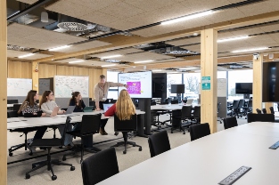A staff member standing up and teaching a group of students sat at a table
